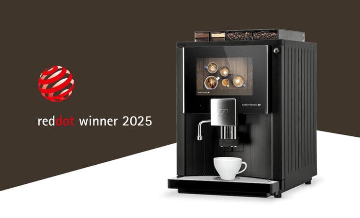 Kaffeevollautomat von Kaffee Partner mit moderner Touchscreen-Oberfläche, ausgezeichnet mit dem Red Dot Design Award 2025. Auf dem Bildschirm sind verschiedene Kaffeespezialitäten zu sehen. Links daneben das Red Dot Winner Logo auf braunem Hintergrund.