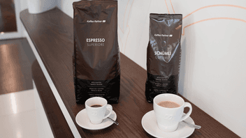 Zwei Kaffeepackungen von Kaffee Partner – Espresso Superiore und Schümli Gourmet – stehen nebeneinander auf einem dunklen Holztresen.