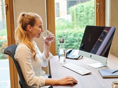 Frau sitzt am Schreibtisch mit einem Glas Wasser in der Hand