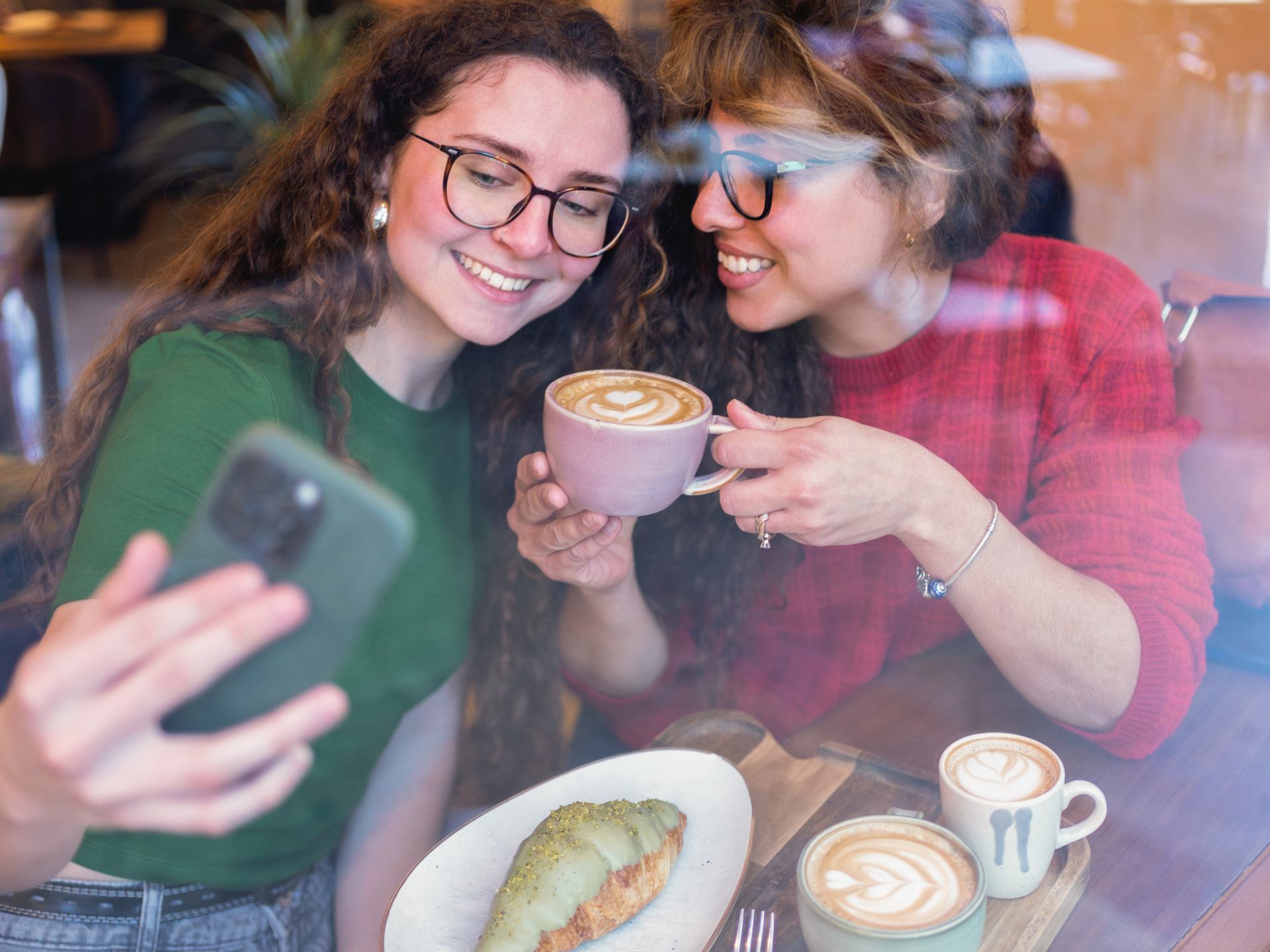Frauen machen Selfie mit Latte Art und Gebäck im Café